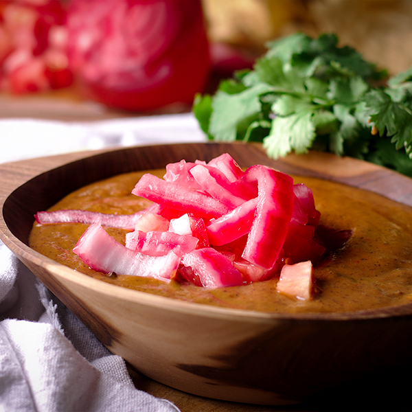 A bowl of black bean soup topped with pickled onions.