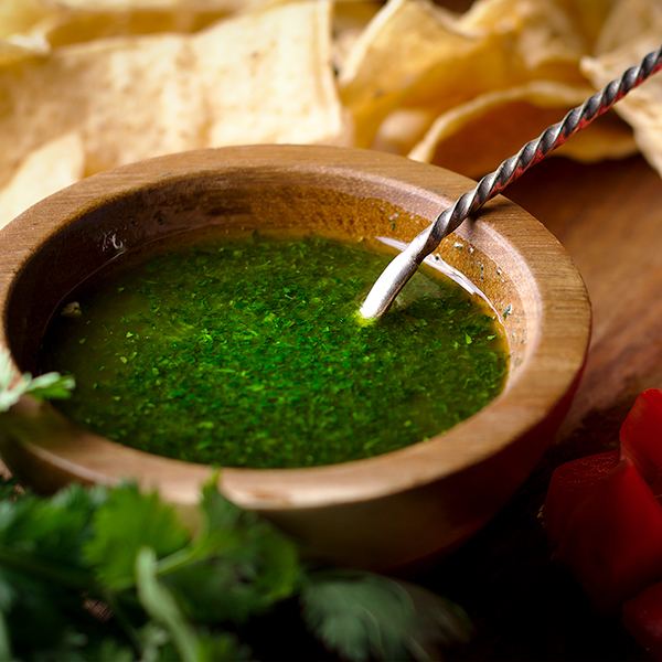 A small bowl of cilantro oil with a spoon, ready to drizzle over black bean soup.