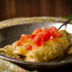Black Bean Enchiladas with Creamy Tomatillo Sauce and chopped tomatoes on a plate ready to eat.