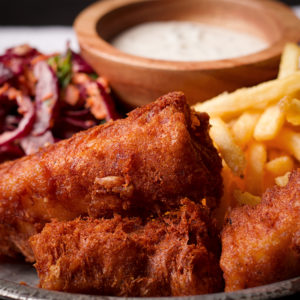 A plate of light and crispy beer battered fried fish with French fries, coleslaw and tartar sauce.