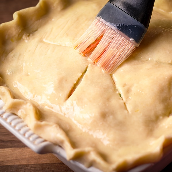 Using a pastry brush to coat the top of the pot pie pastry with egg wash.