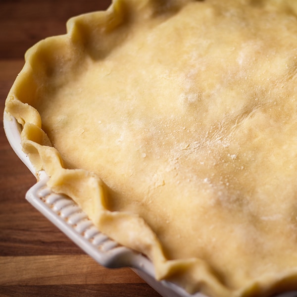 Adding a top crust to the pot pie and crimping the edges of the pastry to seal.