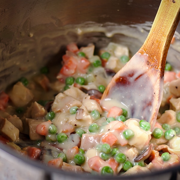 Using a wooden spoon to stir chicken and vegetables into the gravy to make a pot pie filling.