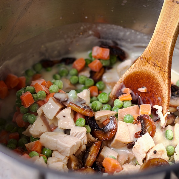 Adding peas and carrots and chunks of chicken to the pot pie gravy.