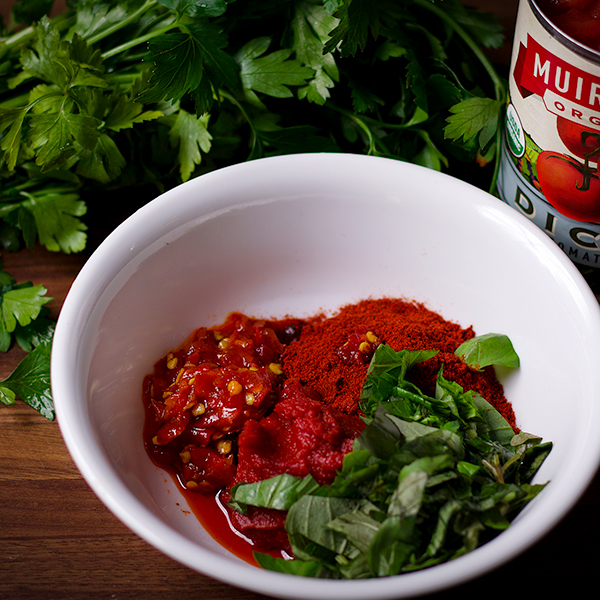 A bowl with Calabrian peppers, paprika, and chopped fresh parsley and basil.