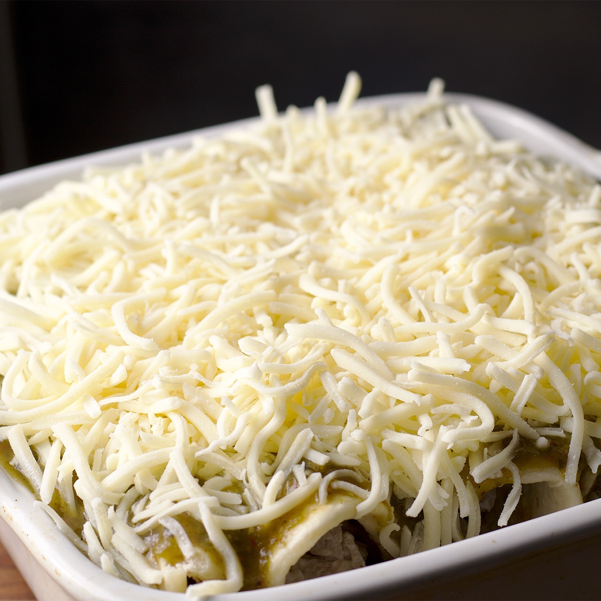 Topping chicken enchiladas with creamy salsa verde and grated cheese.