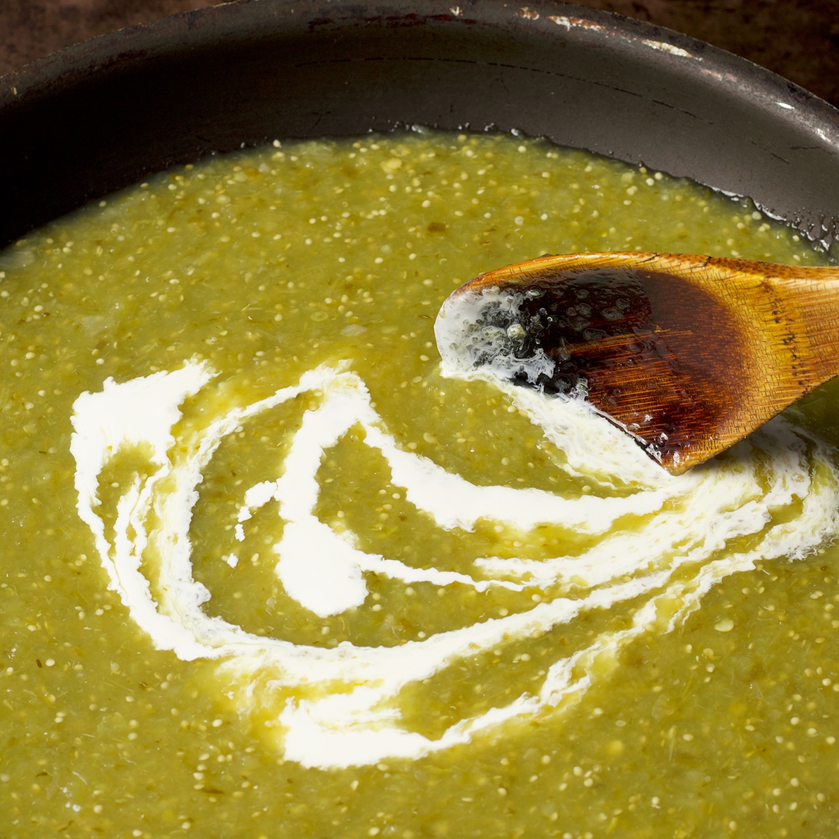 Using a wooden spoon to mix heavy cream into salsa verde.