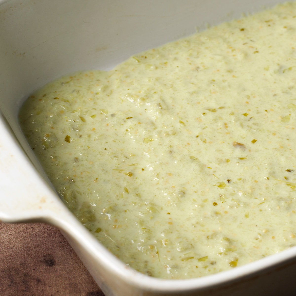 About a half cup of creamy enchiladas verdes sauce spread across the bottom of a baking dish.
