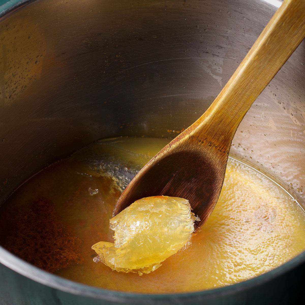 Using a wooden spoon to scrape solidified oil from a stockpot.