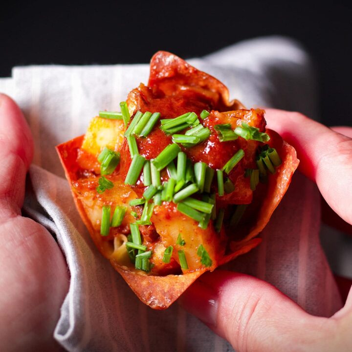 Someone holding a caramelized celery root wonton cup appetizer on a blue cloth napkin.