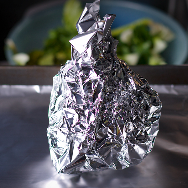 A whole celery root wrapped in aluminum foil, ready to roast.