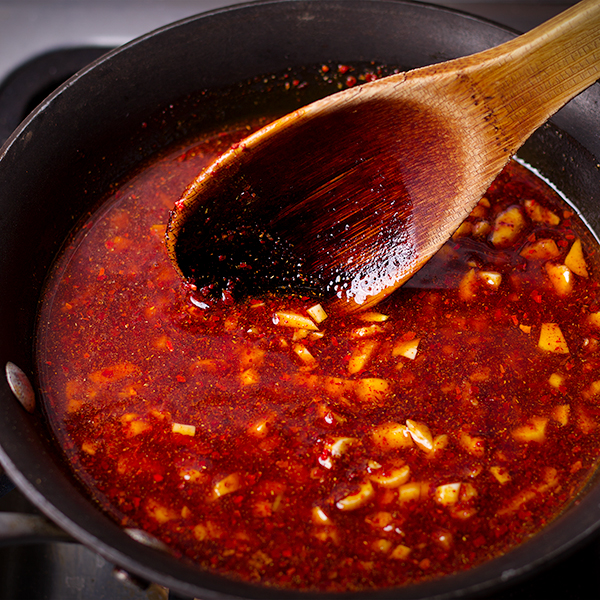 Stirring crispy garlic and Aleppo pepper chili oil in a small saucepan.