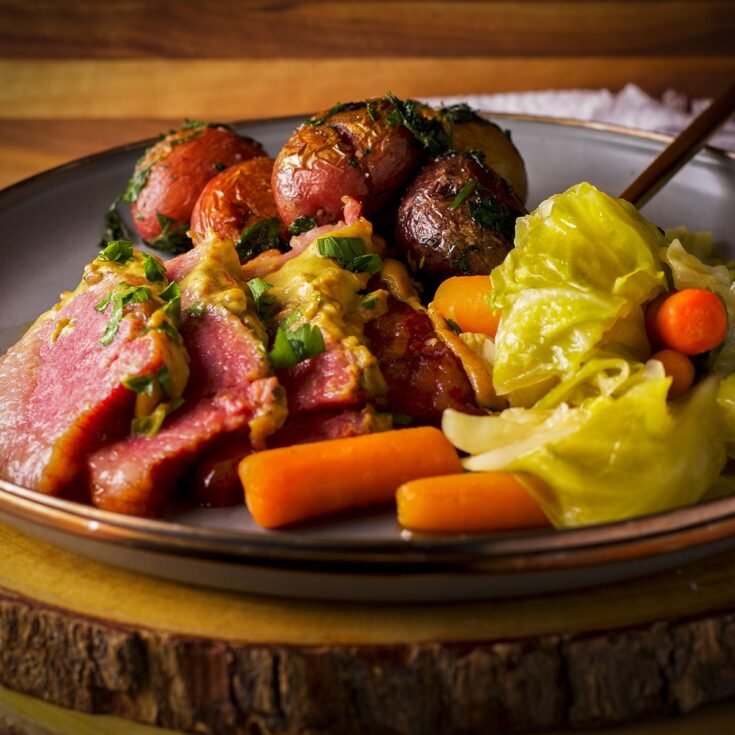 A plate filled with corned beef and cabbage with mustard sauce, carrots, and parsley buttered potatoes.