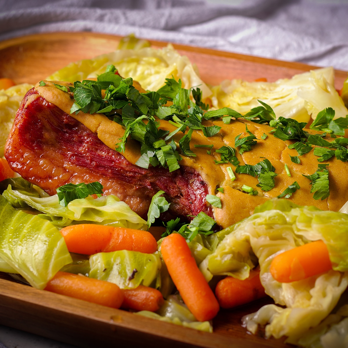 Corned beef covered in mustard sauce and surrounded by cooked cabbage and carrots.