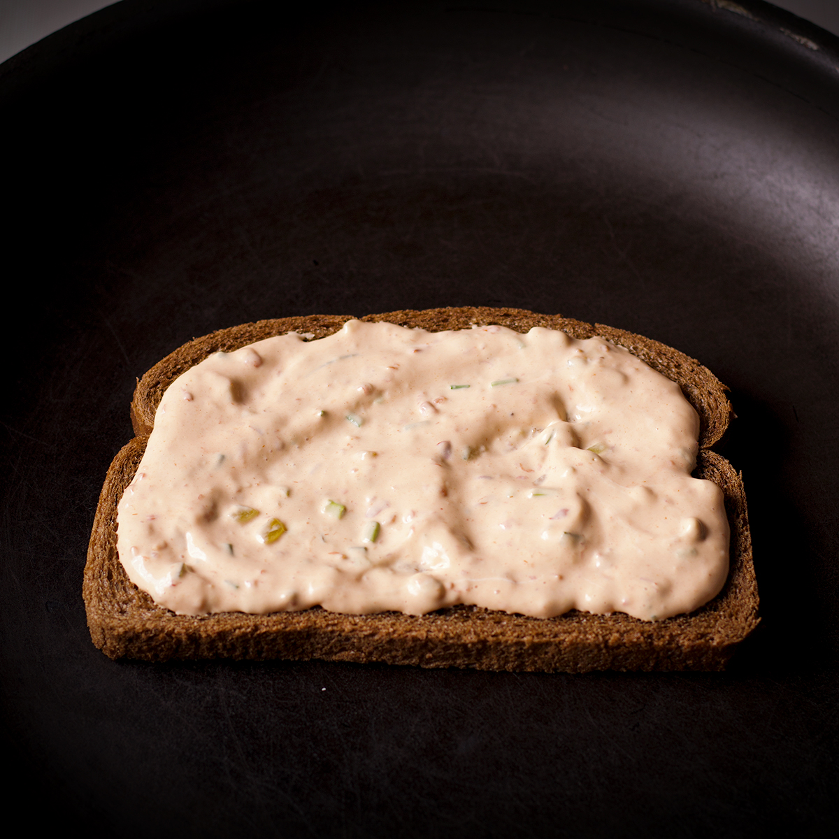 A piece of Rye bread spread with Russian dressing in a skillet.