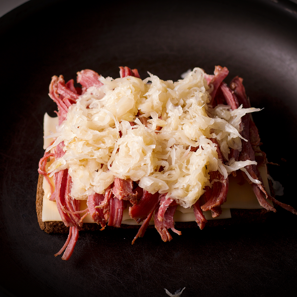 A piece of Rye bread spread with Russian dressing and layered with Swiss cheese and corned beef and Sauerkraut in a skillet.