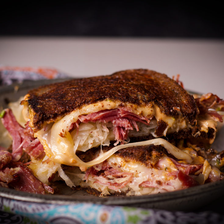 A Reuben Sandwich that's been cut in half, one half stacked onto the other.