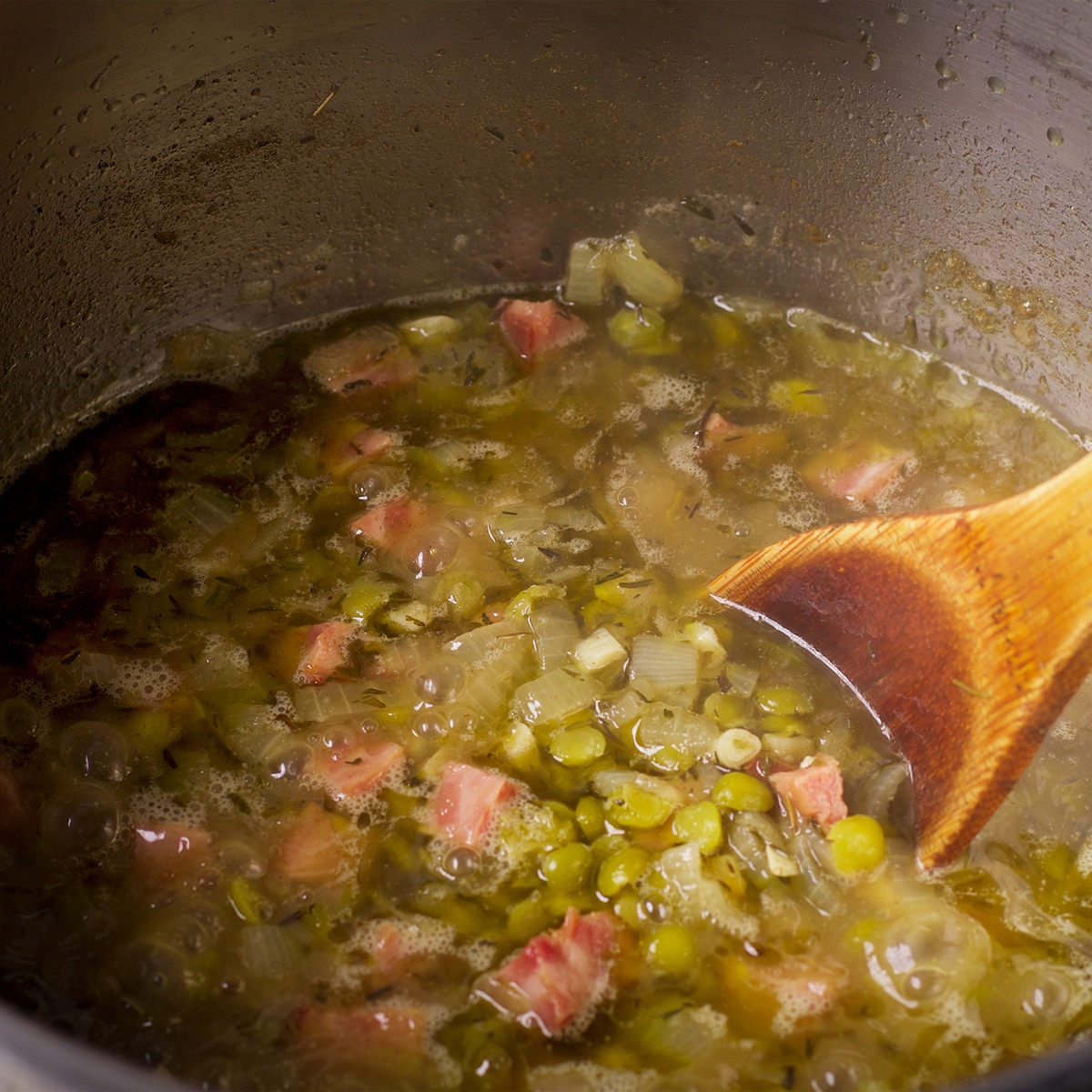 Using a wood spoon to stir a pot of split pea soup while it cooks.