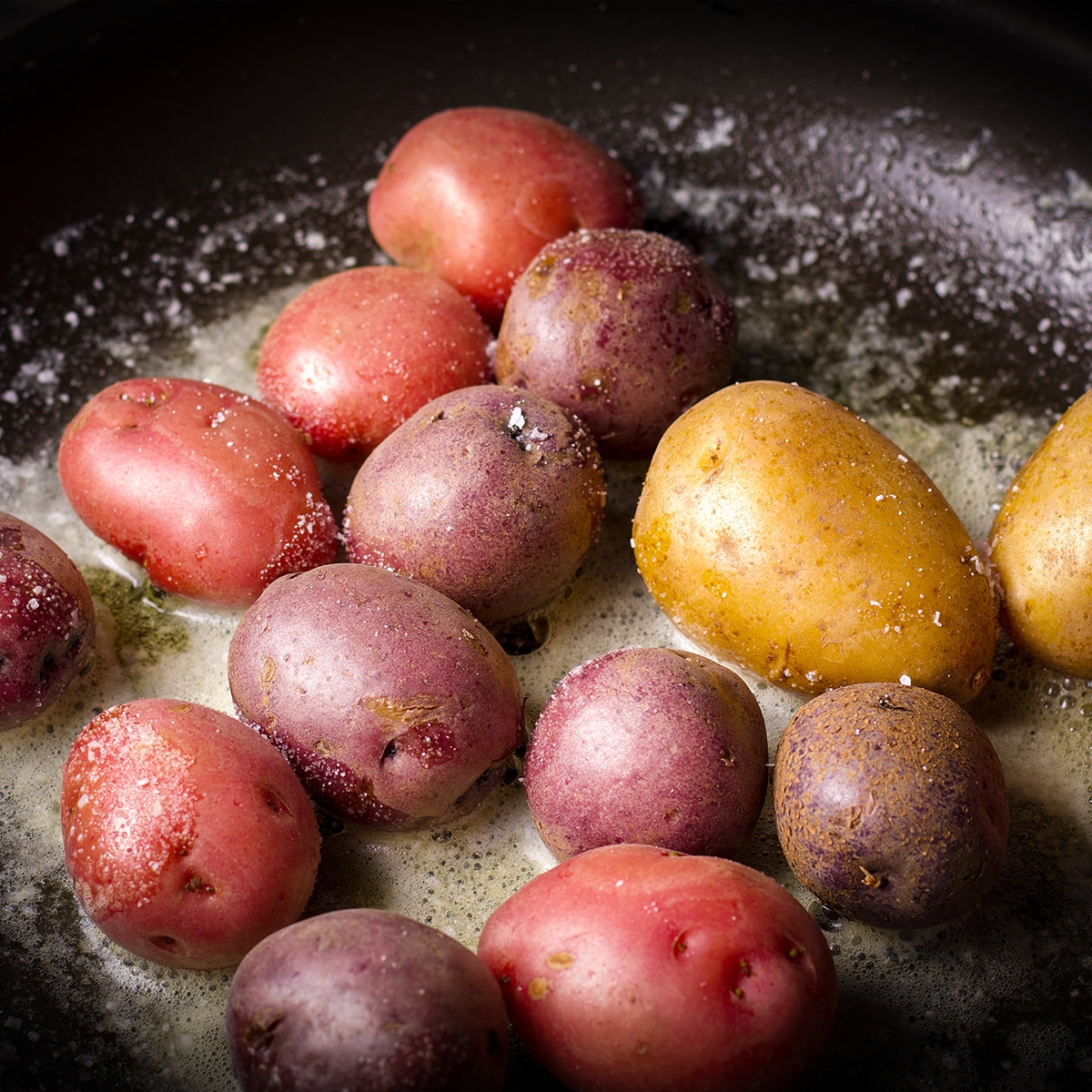Sprinkling salt over small potatoes cooking in butter in a skillet.