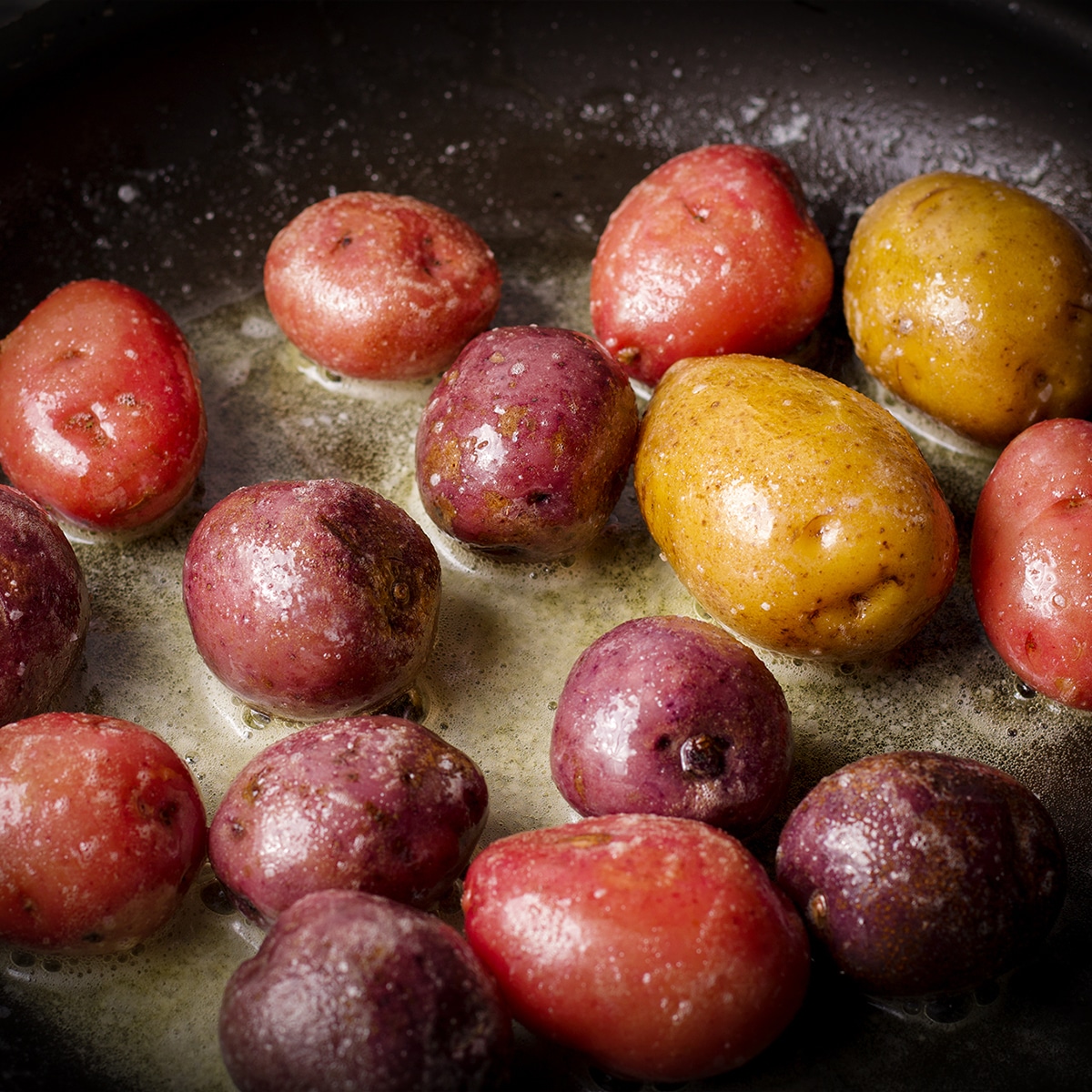 Small potatoes cooking in butter in a black skillet.