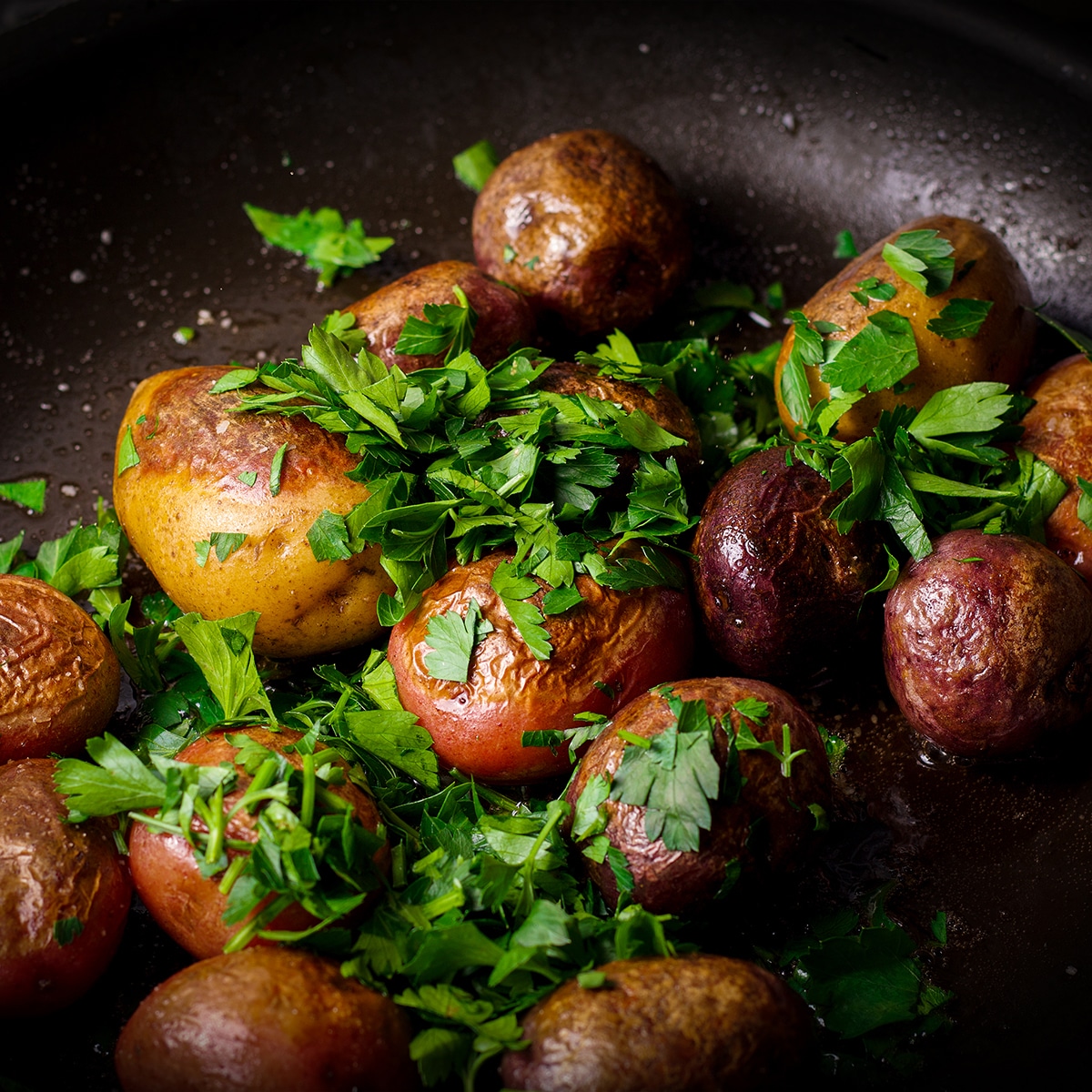 Sprinkling fresh parsley over potatoes while they cook in butter in a skillet.