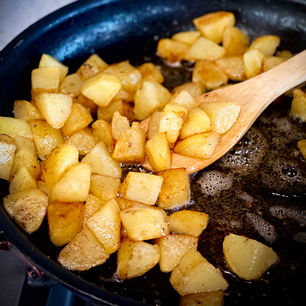 Stirring a pan of crispy fried potatoes.