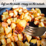 A fork with one crispy fried potato on it and a pan of crispy fried potatoes in the background.
