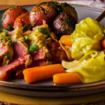 A plate filled with corned beef and cabbage with mustard sauce, carrots, and parsley buttered potatoes.