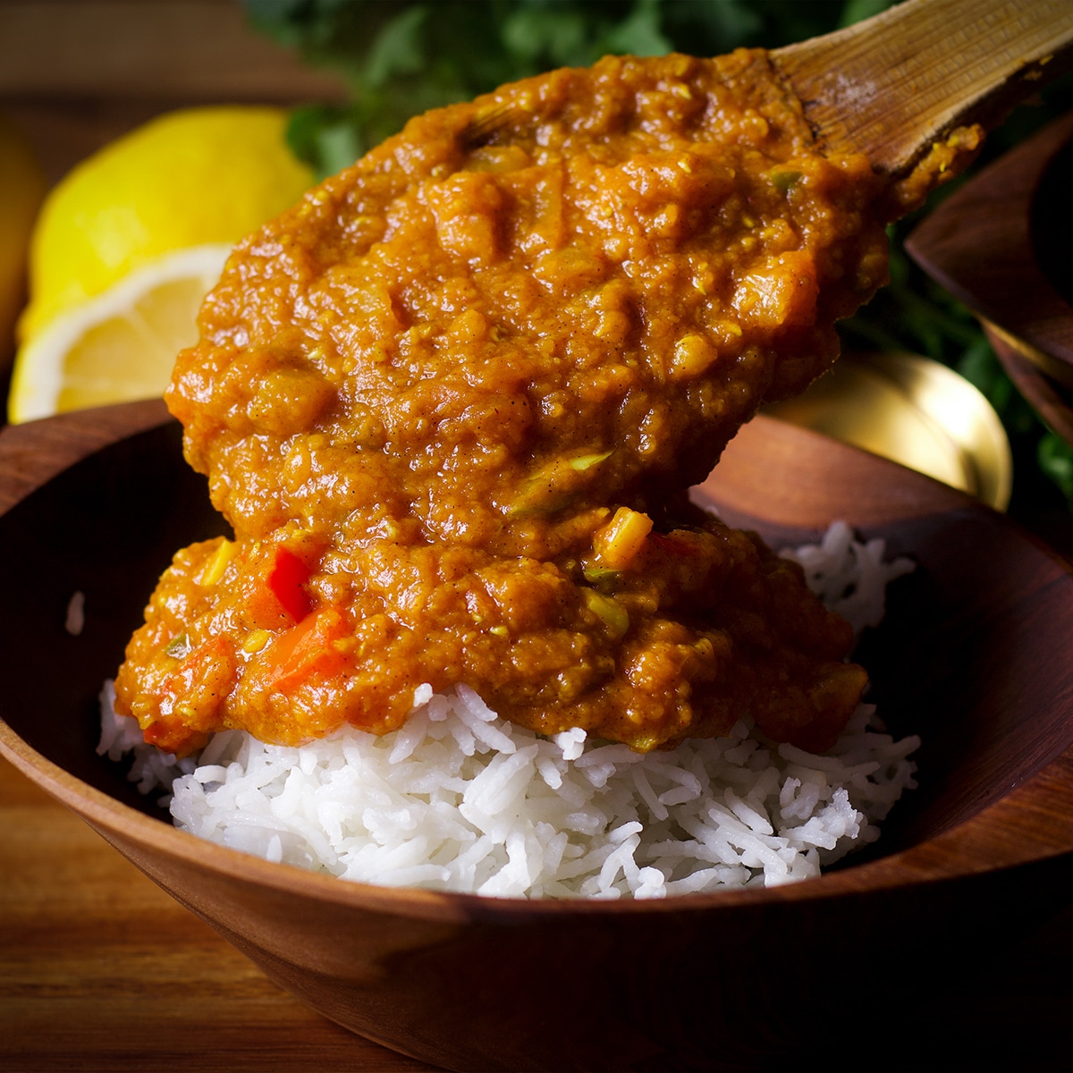 Spooning red lentil dal over a bowl filled with white rice.