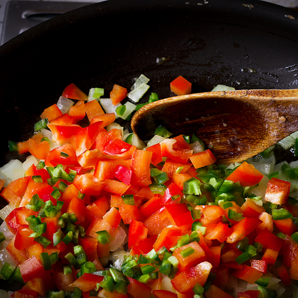 Cooking diced onion, red bell pepper, and jalapeño in a skillet to make lentil dal.