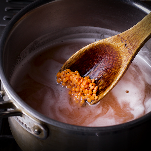 Stiring red lentils into a pot of water.