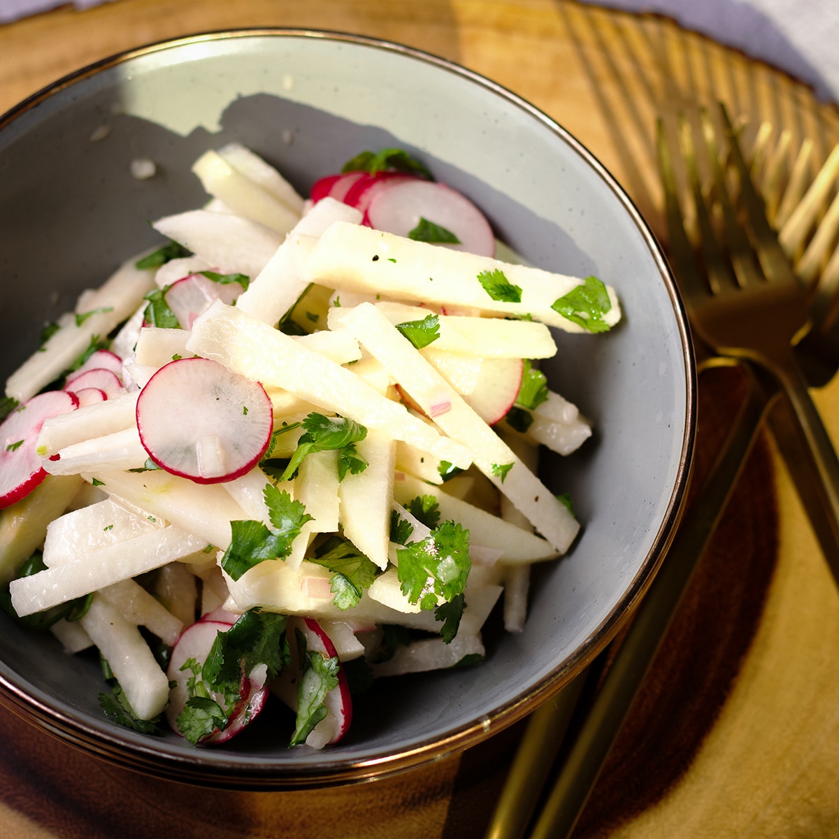 A bowl on a wood serving platter filled with jicama salad with apples.