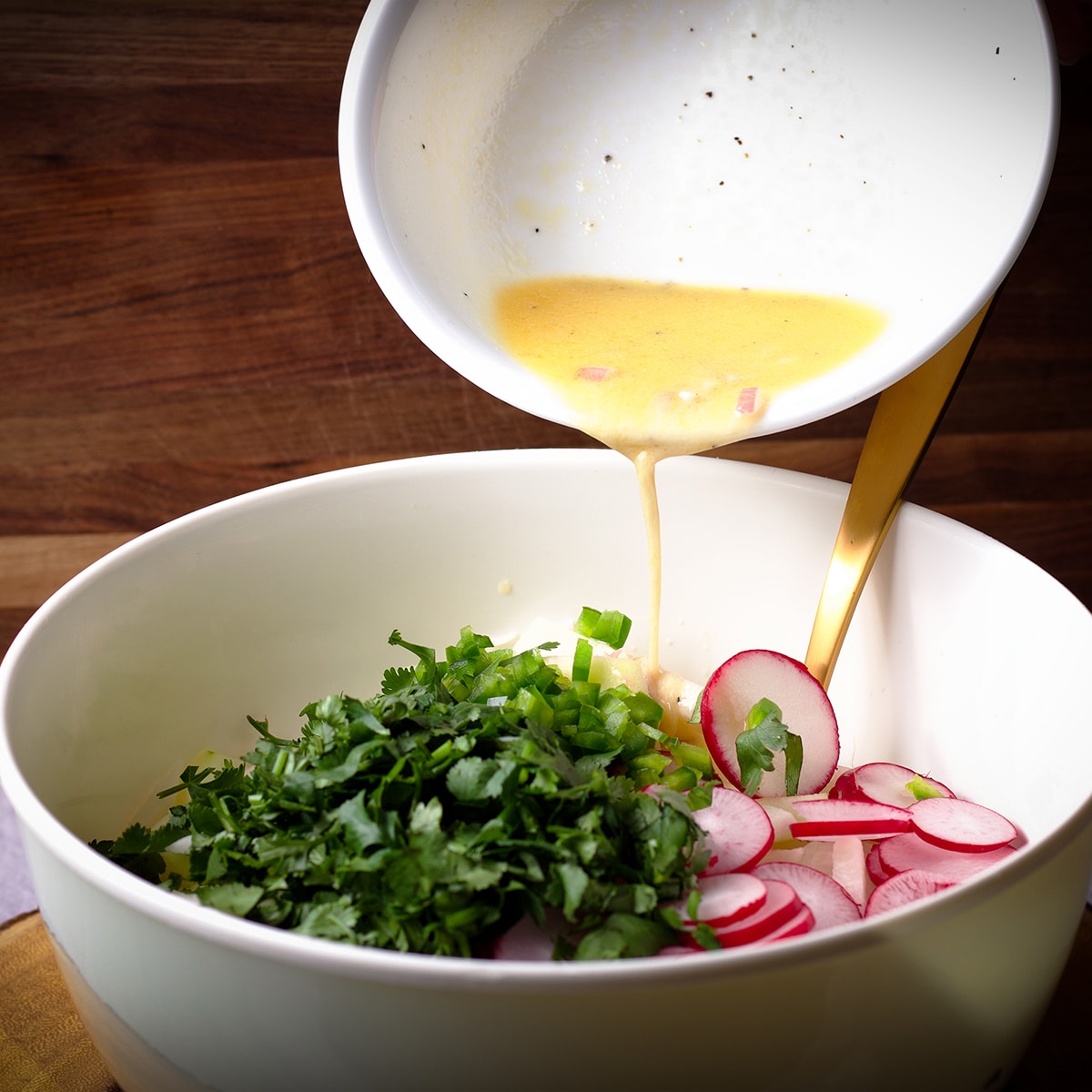 Pouring honey lime dressing over vegetables to make jicama salad.