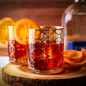 Two glasses on a wood serving board filled with ice and pomegranate margaritas and garnished with orange slices.
