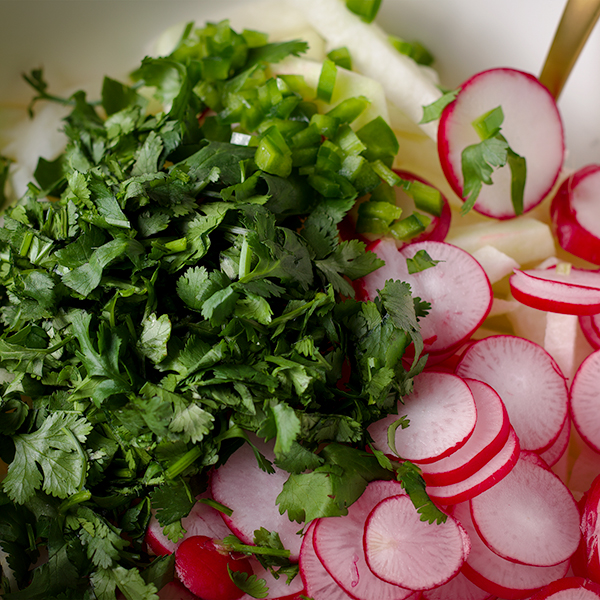 Sliced jicama, radishes, and cilantro in a bowl.