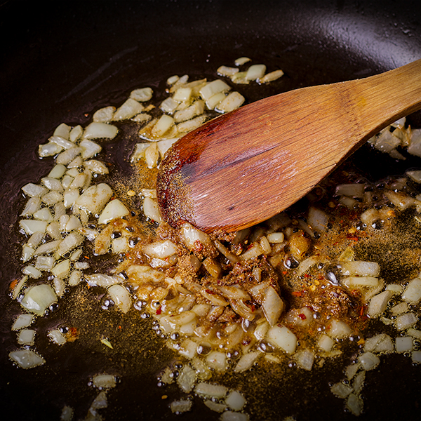 Stirring chopped onions and spices in a skillet.