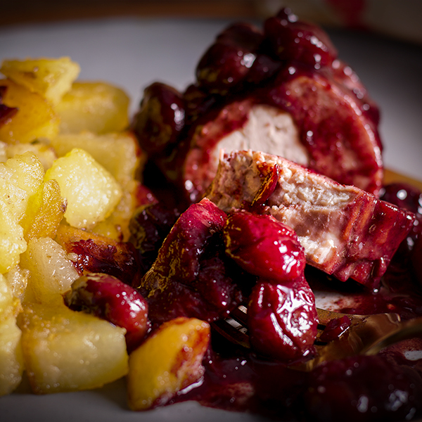 A plate of roast pork with red wine cherry sauce with crispy sautéed potatoes.