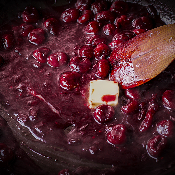 Stirring butter into red wine cherry sauce.