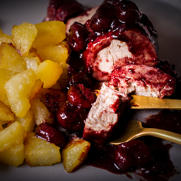 A plate of roast pork with red wine cherry sauce with crispy sautéed potatoes.