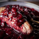 Roasted pork tenderloin on a plate covered in red wine cherry sauce.