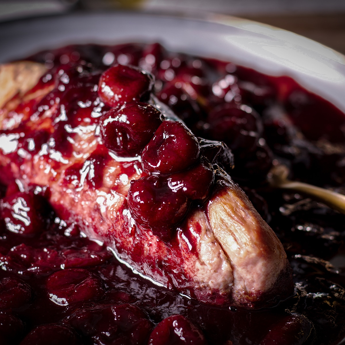 A roasted pork tenderloin on a serving platter smothered with red wine cherry sauce.