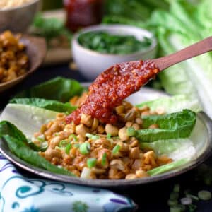 A plate of chicken lettuce wraps with peanuts and chili garlic sauce.