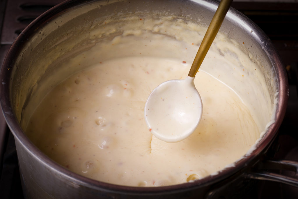 Dipping a spoon into béchamel sauce to show how thick it is. 