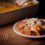 A plate of lasagna bolognese with the pan of lasagna in the background.