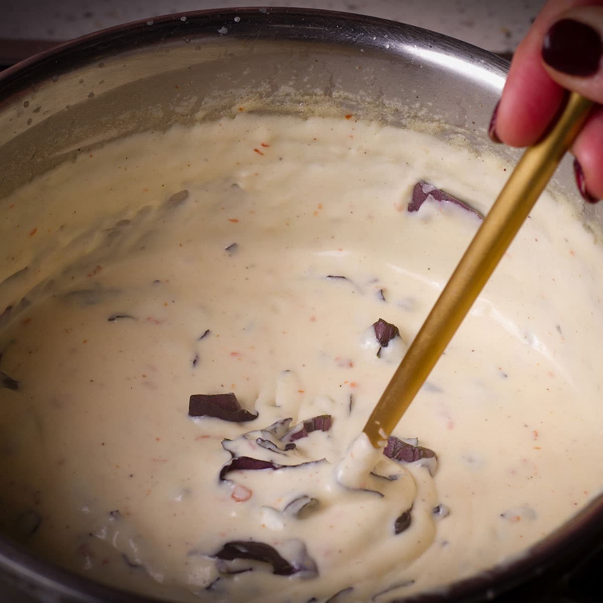 Stirring fresh basil into a saucepan filled with warm bechamel sauce.