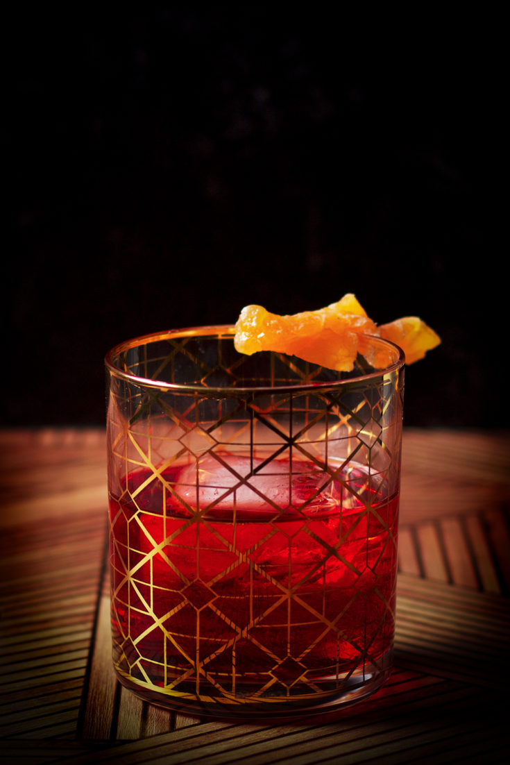 A Boulevardier cocktail, served in a cocktail glass over ice and garnished with an orange twist.
