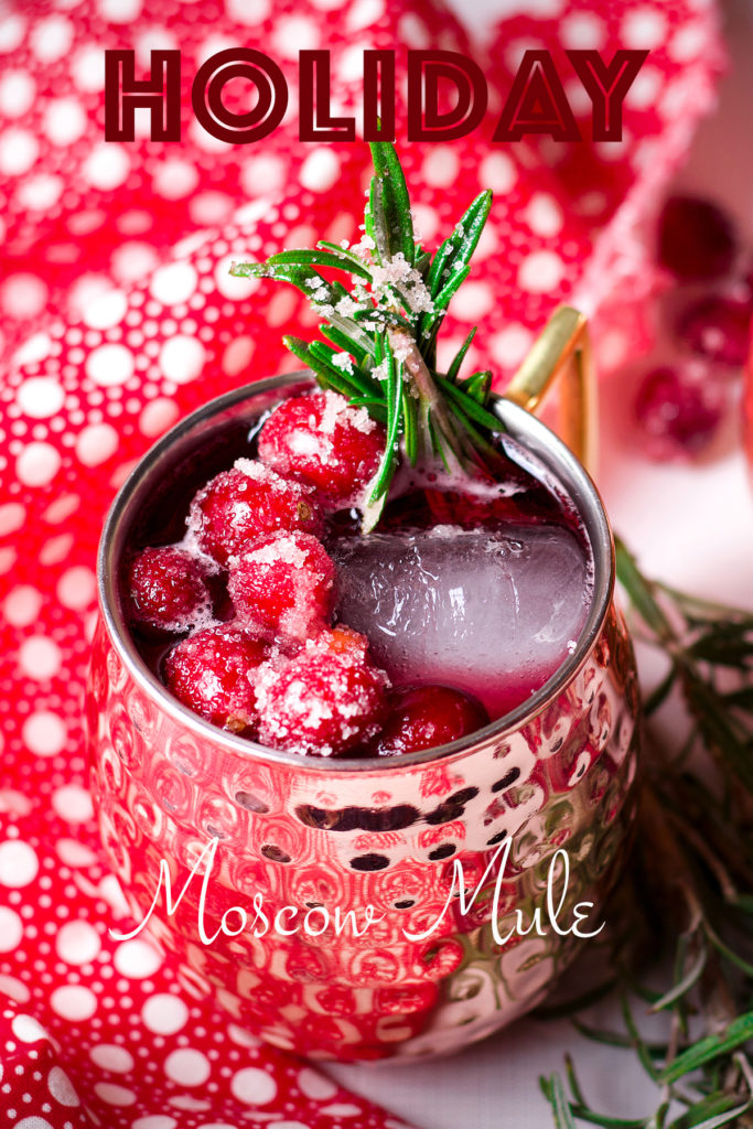 A Cranberry Moscow Mule cocktail in a copper Moscow Mule Mug garnished with sugared cranberries and fresh rosemary.