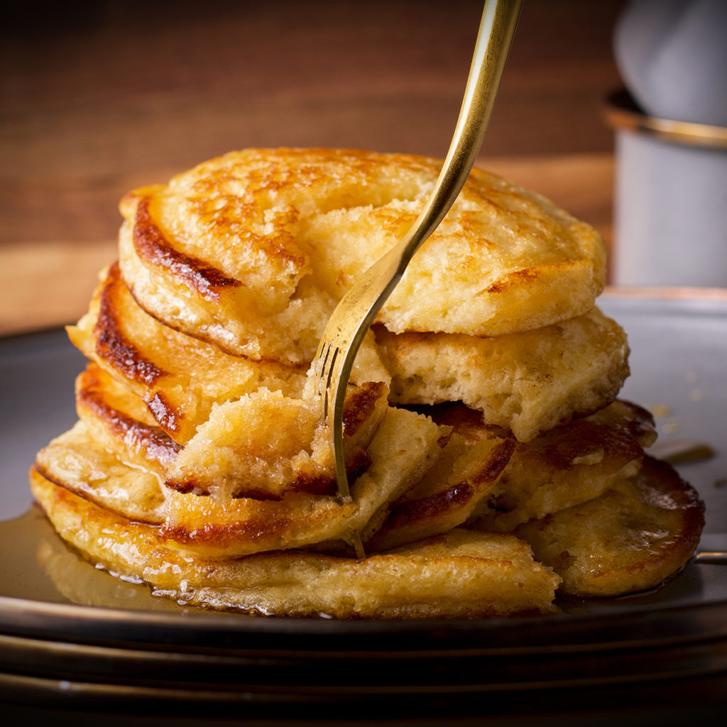 A plate of Everyday Pancakes on a plate, covered in maple syrup, with a fork taking a bite from the stack.