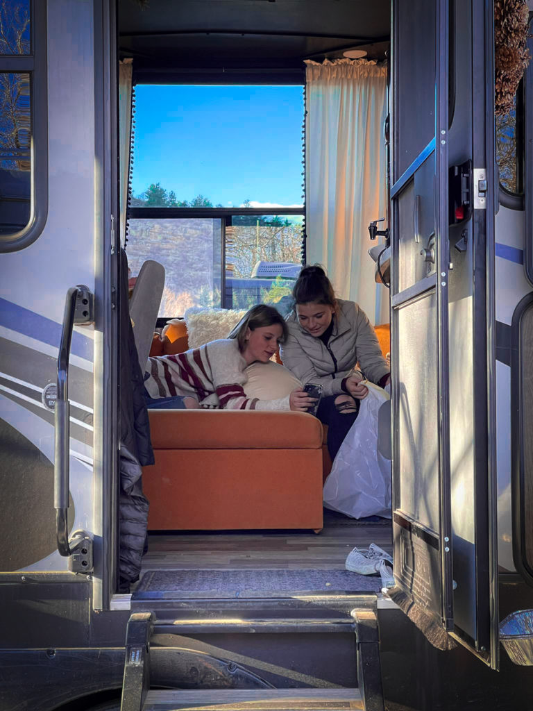 A photo of two girls inside an RV looking at something on their phone.