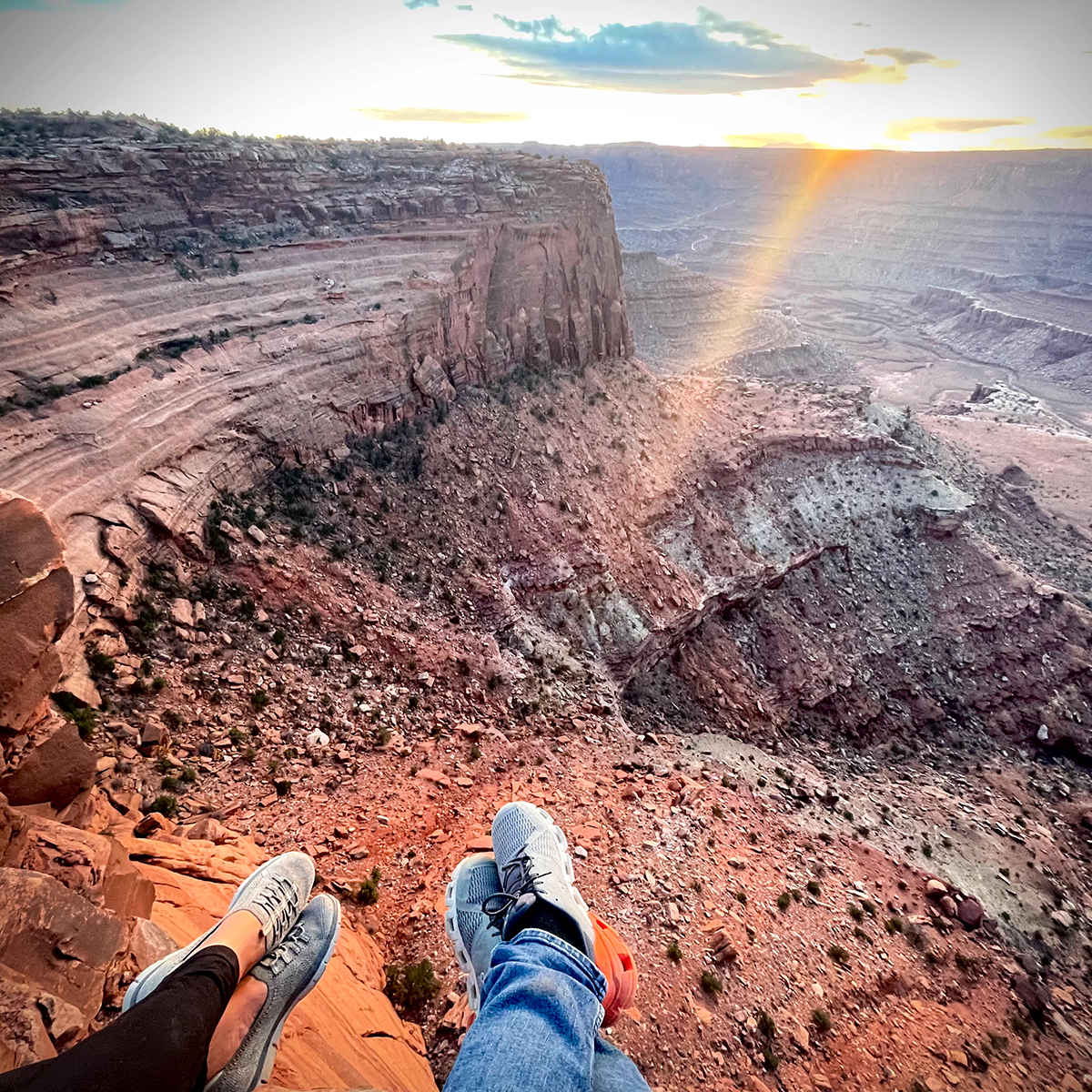 Two people sitting on the edge of a canyon at Dead Horse Point, Utah, with their feet dangling from the edge.